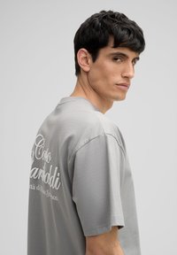 Grijze t-shirt met korte mouwen, voorzien van een ronde hals, een comfortabele pasvorm en een textuurstof. De achterkant toont witte tekst in een cursieve lettertype.