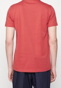 Camiseta de algodón roja con mangas cortas, cuello redondeado y diseño liso. Presenta dobladillos cosidos y una textura suave.