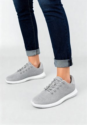 Szare buty sportowe posiadają teksturowaną dzianinową cholewkę, okrągły nosek oraz białe gumowe podeszwy. Mają płaskie sznurowadła i niskoprofilowy fason.