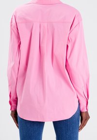 Camicia button-up rosa chiaro a maniche lunghe con colletto e dettaglio a pieghe sul retro. Realizzata in un tessuto morbido, presenta maniche con polsini.