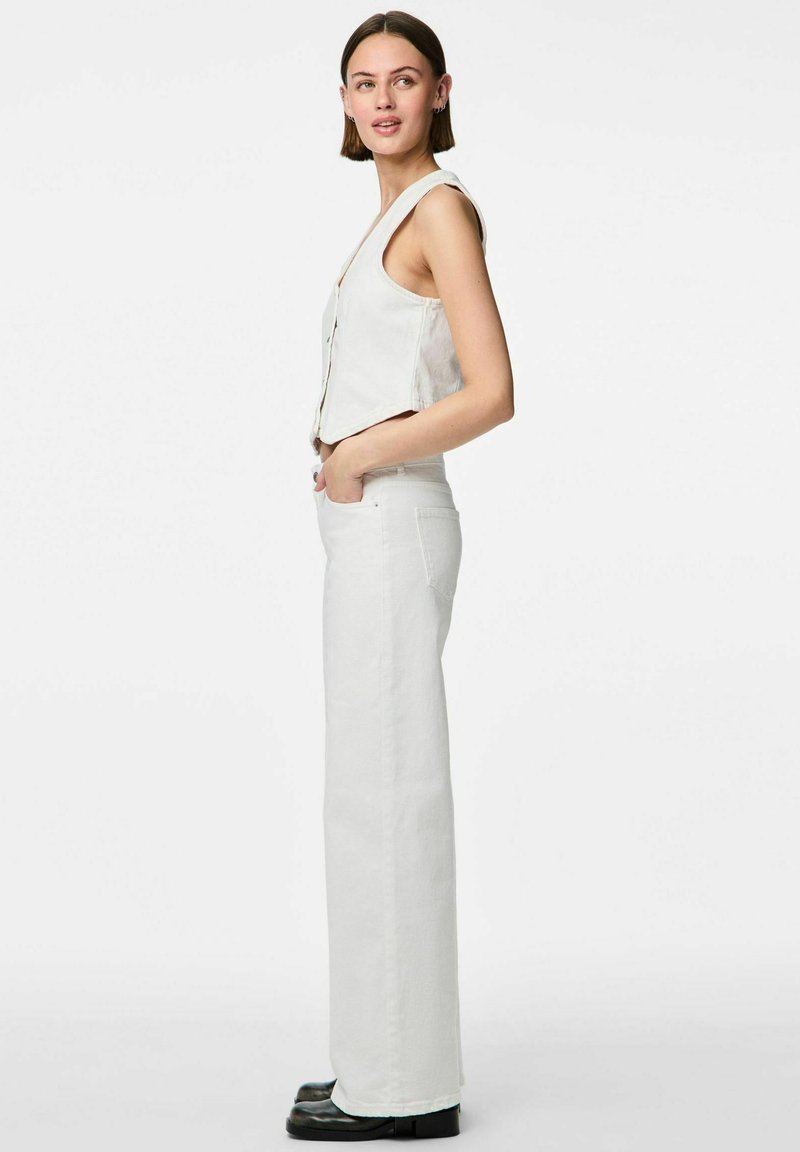 Balti dūnīšanas bikses ar platiem kājiem, apvienotas ar atbilstošu bezpiedurkņu topu, kuram ir priekšējā pogu aizdare un pieguļošs viduklis, novietotas uz gaiša fona.