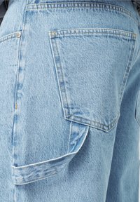 Vaaleansiniset farkut, joissa on suuri sivutasku ja kontrastommat saumat. Kangas on teksturoitu ja haalistuneen näköinen.