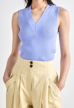 Ljust blå ribbad ärmlös topp med V-ringning. Kombinerad med högmidjade beige byxor med dubbla knapppdetaljer och sidofickor.