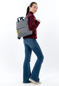 Hall kanga seljakott kahe kandekäepideme, õlarihmade, tõmblukuga ees tasku ja kollase tõmbluku tõmbajaga; mudeli peal eksponeeritud.