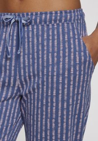 Plave trenirke s vertikalnim ružičastim prugama, s elastičnim pojasom sa mašnom, bočnim džepovima i mekim materijalom.