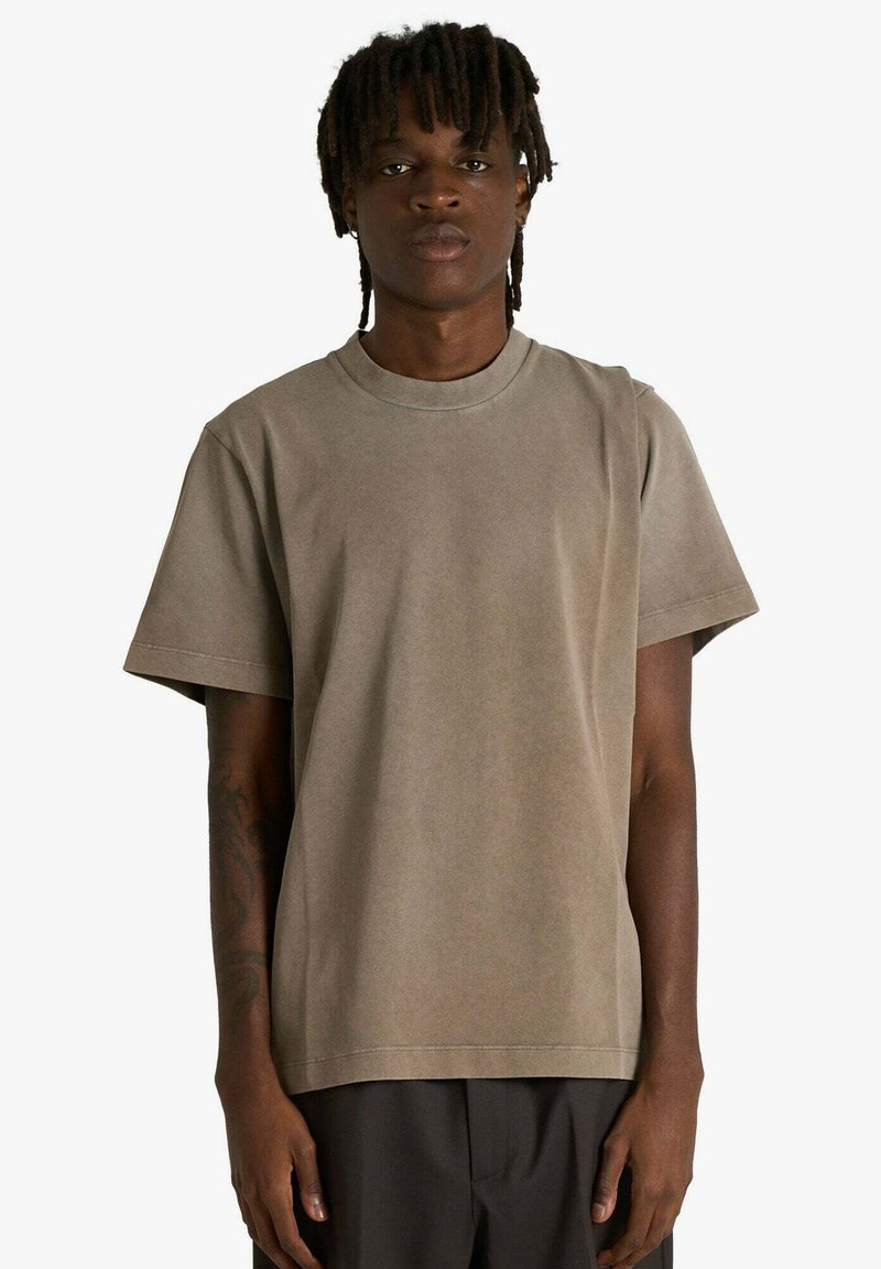 T-shirt marrone in cotone con vestibilità comoda, maniche corte, scollo rotondo e trama liscia, indossata da una modella su sfondo bianco.