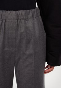 Pantalon gris texturé avec une taille élastique et des poches latérales, associé à un haut noir à manches longues.