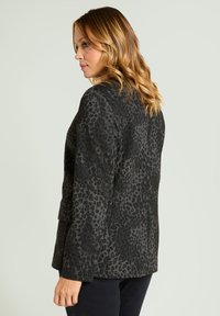 Blazer negro texturizado con diseño de estampado de leopardo, con mangas largas y ajuste estructurado, mostrado desde atrás sobre un fondo claro.