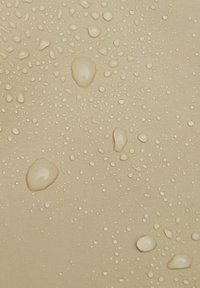 Beige textilní látka se strukturou a kapkami vody různé velikosti na povrchu, která ukazuje voděodolné vlastnosti.