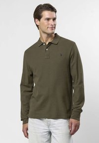 Olivgrön långärmad pikétröja med tvåknappslinning och subtil broderad logotyp på bröstet; muddade ärmslut och slät tygstruktur.