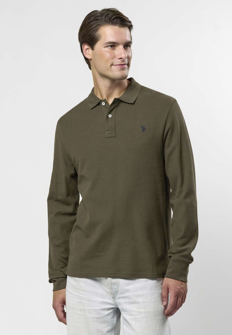 Olivgrön långärmad pikétröja med tvåknappslinning och subtil broderad logotyp på bröstet; muddade ärmslut och slät tygstruktur.