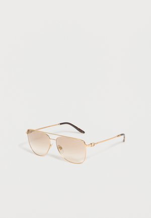 Ochelari de soare aviator cu ramă metalică aurie, lentile degradate maro deschis și vârfuri negre la brățări, așezați pe o suprafață albă.