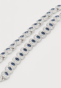 Silver bracelet featuring oval blue stones surrounded by small clear crystals, linked in a repeating pattern. Smooth, polished texture.