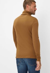 Maglione a collo alto marrone a maniche lunghe con una texture liscia e un design aderente, abbinato a jeans blu. Focus su uno stile minimalista.