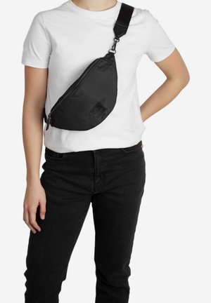 Sort stof crossbody tas med en buet design, lynlåslukning, justerbar strop og et tekstureret logo på fronten.