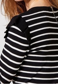 Svart och vit randig tröja med volangdetaljer på axlarna och dragkedja i ryggen. Mjukt stickad textur, figurnära design.