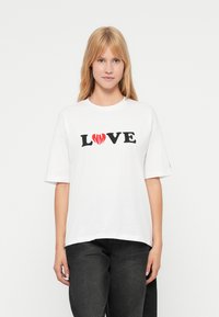 Λευκό βαμβακερό μπλουζάκι με κοντά μανίκια, στο οποίο αναγράφεται "LOVE" με μαύρα γράμματα και διακοσμείται με μια κόκκινη καρδιά. Κανονική εφαρμογή, σχέδιο με στρογγυλή λαιμόκοψη.