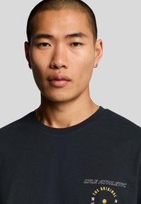Marineblå bomulls t-skjorte med rund hals og liten frontgrafikk med tekst og et sirkulært design i gul broderi.