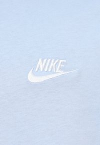 Ανοιχτό μπλε βαμβακερό μπλουζάκι με κεντημένο λευκό λογότυπο Nike στο μπροστινό μέρος. Το ύφασμα έχει ομαλή υφή και κλασικό στρογγυλό λαιμόκοψη.