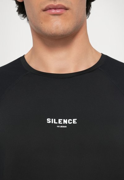 Melnas īsām piedurknēm krekls, izgatavots no gludas auduma, ar apaļu kakla izgriezumu un baltu uzdrukātu tekstu "SILENCE" uz priekšpuses.