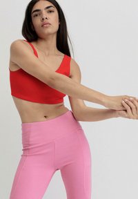 Rotes Cropped-Top aus elastischem Stoff, kombiniert mit hochtaillierten pinken Leggings. Glatte Textur, simples Design, enganliegende Silhouette, ohne Muster.