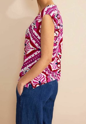 T-shirt à manches courtes en rose vif avec des motifs floraux abstraits, fabriqué dans un tissu lisse. Associé à un jean large bleu.