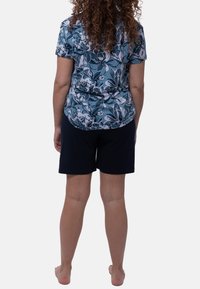 Camicia a maniche corte floreale azzurro chiaro abbinata a pantaloni corti di colore blu scuro. La camicia presenta un orlo arrotondato e un tessuto morbido e testurizzato.