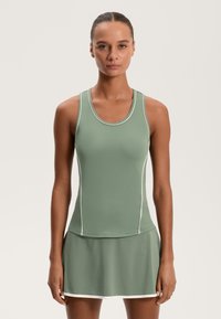 Zöld sportos ujjatlan top fehér díszítéssel, testhezálló kialakítással és bővülő szoknyával. Sima textúra, kerek nyakú és ujjatlan stílus.