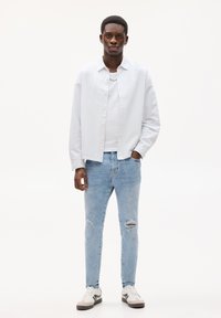 Bijela i plava prugasta košulja, bijela majica, svijetloplave traperice s poderotinama i bijele tenisice s nijansama sive i crne. Opusten izgled.