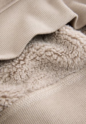 Beige sweaterstof med ribbet tekstur på det øverste lag og blødt, fluffy for indeni. Sømme detaljer synlige langs kanterne.