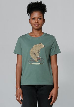 T-shirt en coton vert présentant une illustration d'un ours brun faisant du vélo rouge, avec un col rond classique et des manches courtes.