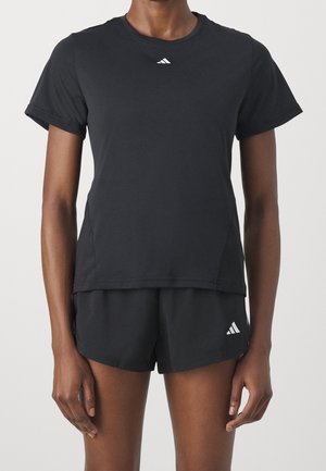 Person iført sort kortærmet sportstrøje og matchende shorts med små hvide Adidas-logoer på brystet og venstre ben.