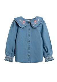 Camicia di denim azzurro chiaro con un ampio colletto volant, ricami floreali e chiusura frontale con bottoni. Maniche a sbuffo con polsini arricciati.