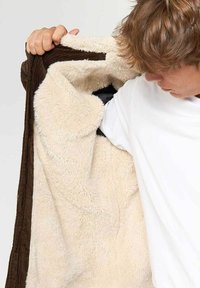Creamfarvet, fluffy fleecejakke med brun kordfløjlstrim; åben for at vise det bløde indre for. Regulær pasform med lange ærmer.