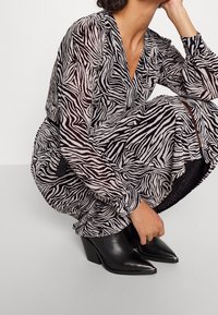 Vestido a rayas de cebra en blanco y negro con mangas largas, puños fruncidos y un escote en V profundo, combinado con botas de tacón negro y punta afilada.