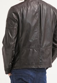 Brun läderjacka med en slät yta, med en strukturerad design, långa ärmar och detaljerad sömnad längs sömmarna.