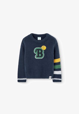 Mørkeblå strikket sweater med et grønt bogstav B og en gul tennisbold foran samt gule, grønne, hvide og mørkeblå striber på højre ærme.