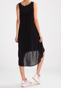 Černé bezrukávové šaty s řasením, délka po lýtka, poloprůhledný překryv, kombinované se světle růžovými sportovními botami s bílými akcenty.