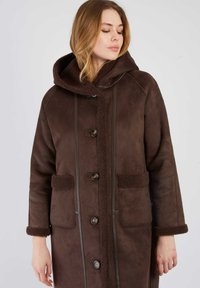 Brązowy płaszcz z sztucznego zamszu z kapturem, z guzikami z przodu oraz teksturowanym, polarowym wykończeniem kołnierza i kieszeni. Posiada kontrastowe szwy.
