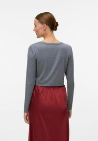 Maglia grigia a maniche lunghe con una vestibilità comoda e scollatura rotonda, abbinata a una gonna rossa fluida con vita arricciata. Tessuto dalla superficie liscia.