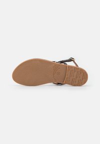 Suela de goma marrón de una sandalia con un patrón de agarre texturizado, que presenta correas negras y acentos de hardware dorado.