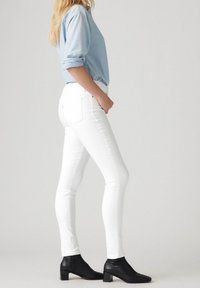 Jeans slim fit blancos combinados con una camisa azul clara, con mangas enrolladas y botas negras hasta el tobillo. Diseño simple, textura suave.