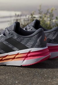 Paire de chaussures de course grises et noires avec des semelles rembourrées roses et orange reposant à l'extérieur sur le trottoir.