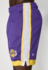 Șorturi de baschet din plasă violet cu dungi laterale albe și galbene, având logo-ul "Los Angeles Lakers" și un brâu elastic cu șnur.