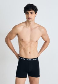 Schwarze Boxershorts aus Baumwolle mit einem weißen, markierten Bund. Die Passform liegt eng am Körper und hat eine glatte Textur.