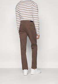 Brązowe bawełniane spodnie o prostych nogawkach, zestawione z pasiastą koszulą z długim rękawem i białymi trampkami. Widoczny minimalistyczny detal z tyłu.