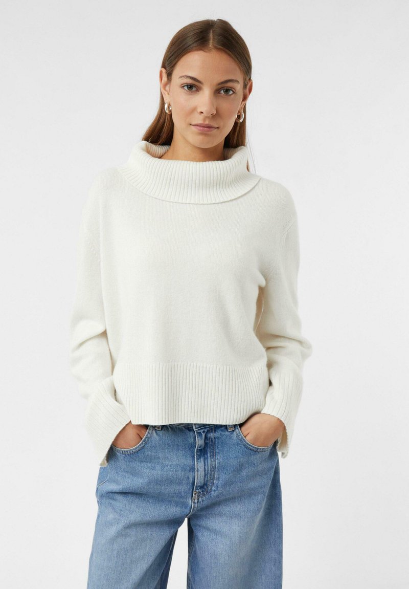 Weißer, rib-knit Pullover mit weitem Kragen und langen Ärmeln, kombiniert mit blauen Jeans. Der Stoff wirkt weich und leicht strukturiert.