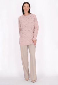 Helles rosa, gestricktes Sweatshirt mit einem Rautenmuster, langen Ärmeln und einem lässigen Schnitt, kombiniert mit beigen, weit geschnittenen Hosen und nude Farbene Schuhen.
