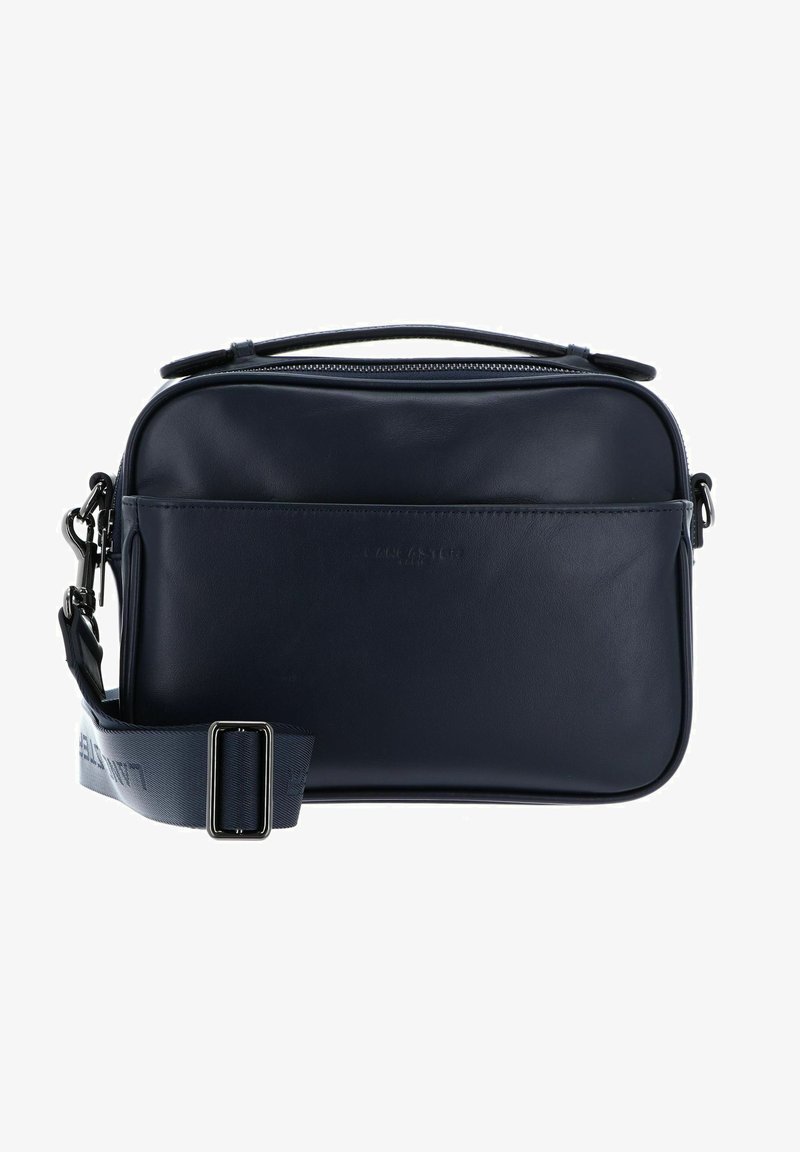 Sac bandoulière en cuir bleu marine avec fermeture éclair, bandoulière réglable et texture lisse ; présente un logo en relief à l'avant et un design minimaliste.