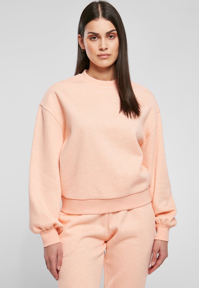 Sudadera de melocotón claro con cuello redondo y mangas abullonadas; hecha de un tejido suave con puños y dobladillo de punto. Combinada con pantalones a juego.